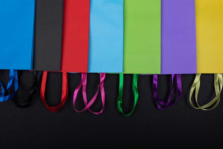 Flat lay of multicolored paper bags with ribbon handles on a dark surface.