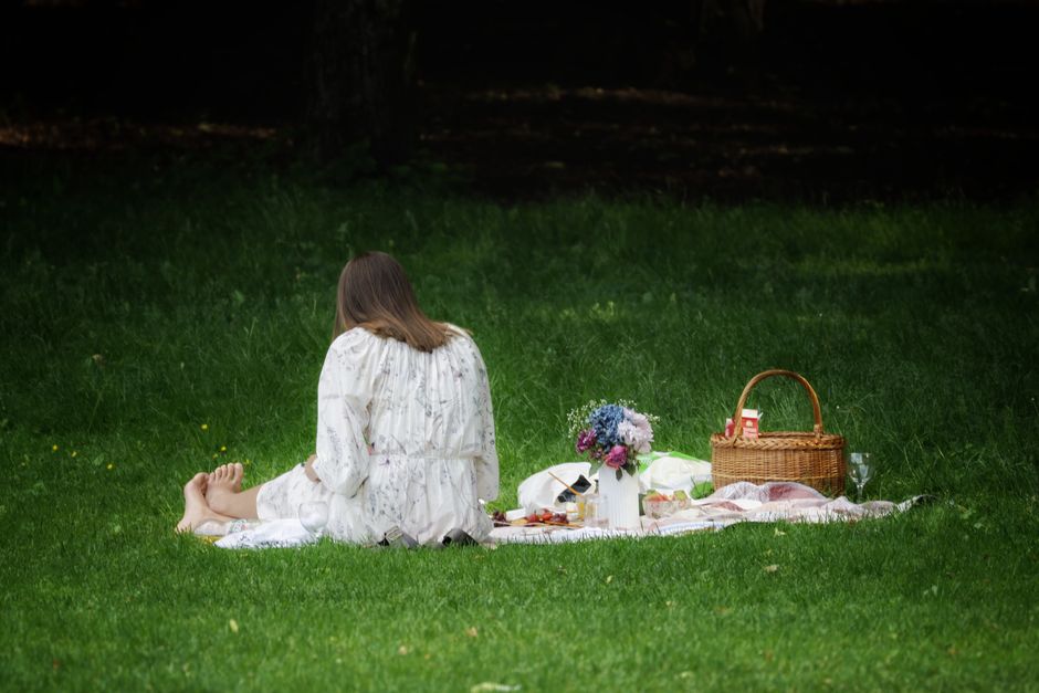 A woman enjoys a peaceful picnic in Oslo, surrounded by nature, flowers, and a basket.