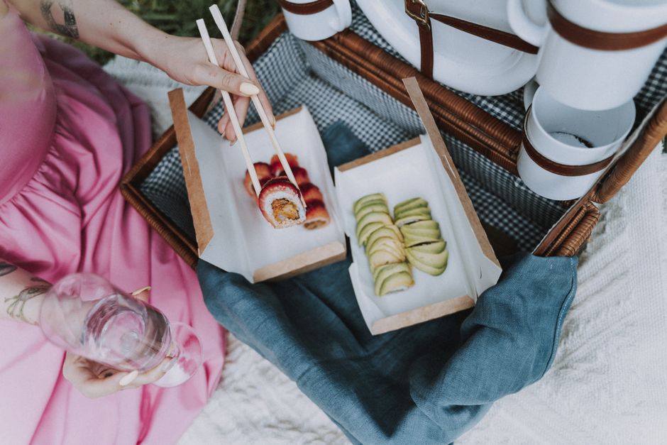 A woman enjoys sushi and wine outdoors, highlighting a chic picnic experience.