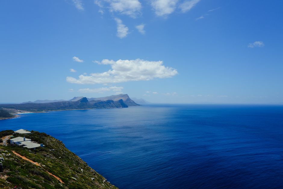 Breathtaking view of a rugged coastline and clear blue ocean under a bright sky filled with clouds.