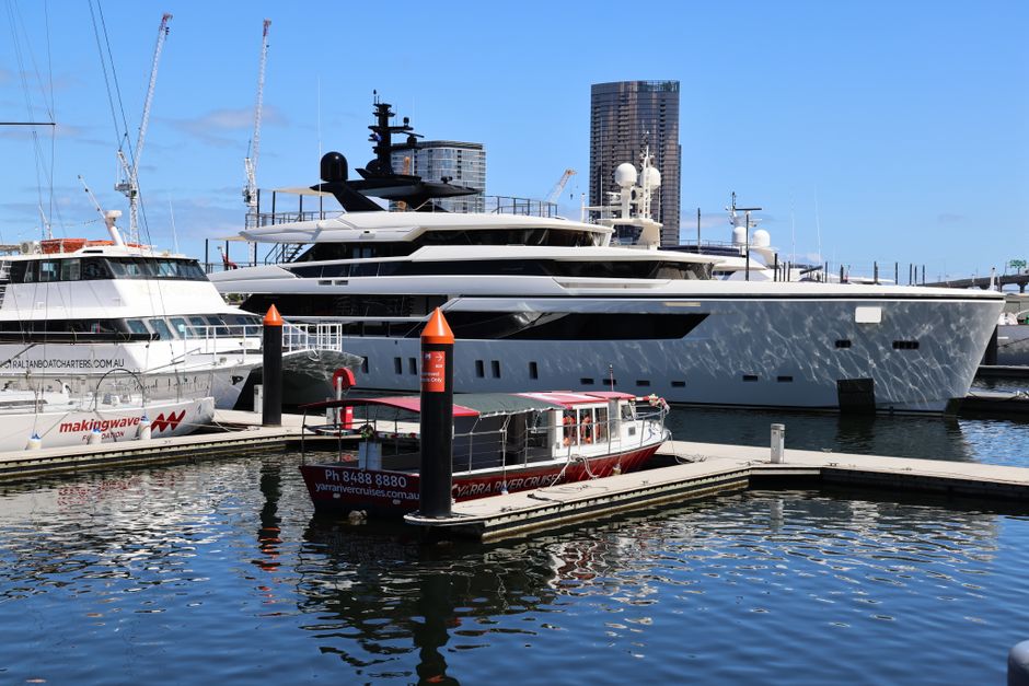 A view of luxury yachts and a small boat docked at a marina on a sunny day.