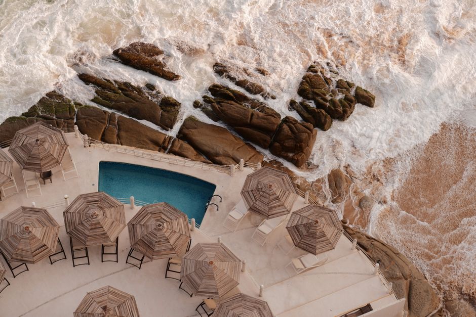 Stunning aerial view of a pool with beach umbrellas beside rocky Acapulco shore.