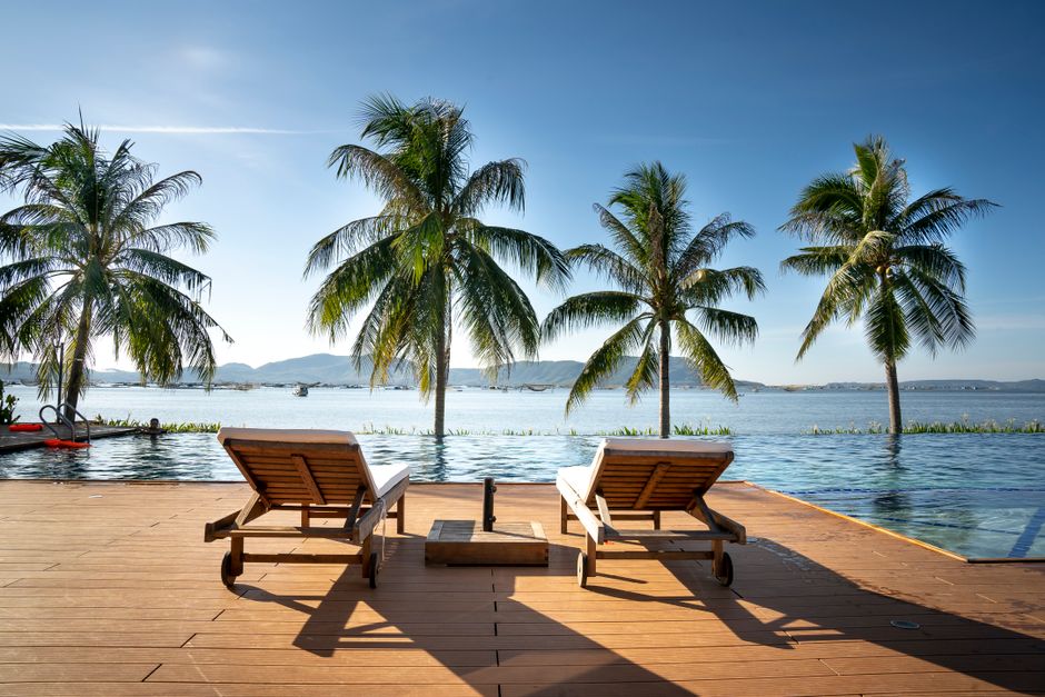 Picturesque scene of wooden pier with deckchairs and palm trees near calm sea in sunny day