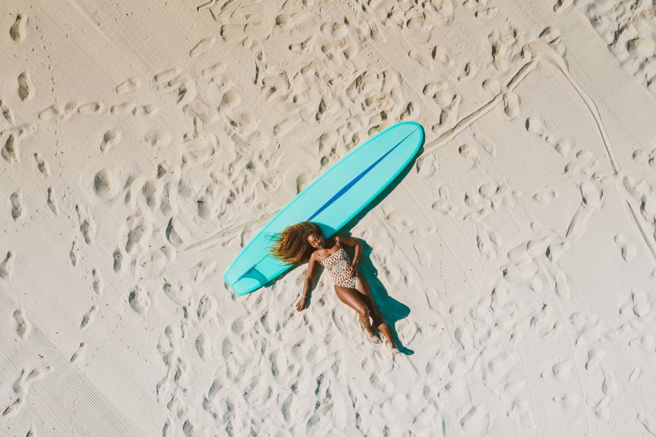 Top view of a woman in leopard swimwear lying on a sandy beach with a surfboard. Perfect summer leisure scene.