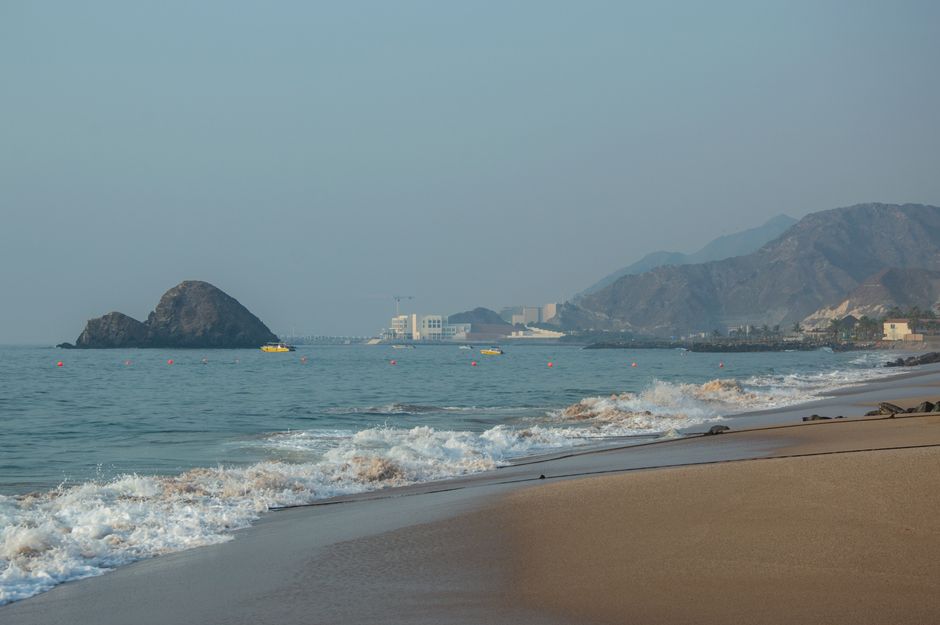 Peaceful beach scene with gentle waves, mountain backdrop, and clear horizon.