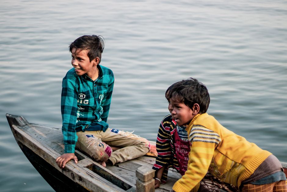 Two boys enjoying a serene boat ride on the Ganges River in Varanasi, India.
