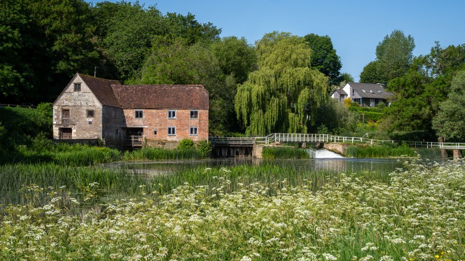 Charming view of a historic mill by a river in the English countryside, surrounded by lush