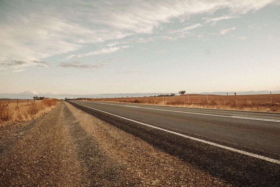 A serene stretch of highway through expansive dry fields under a cloudy sky.