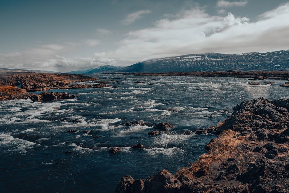 Majestic river flowing through rocky terrain in Iceland, with distant snowy mountains.