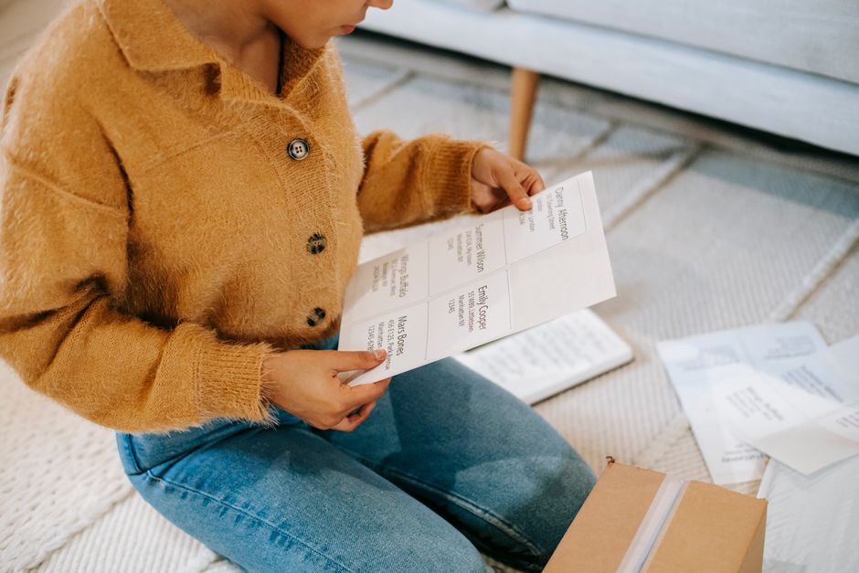 From above of crop anonymous female in trendy soft beige cardigan and jeans reading data on paper