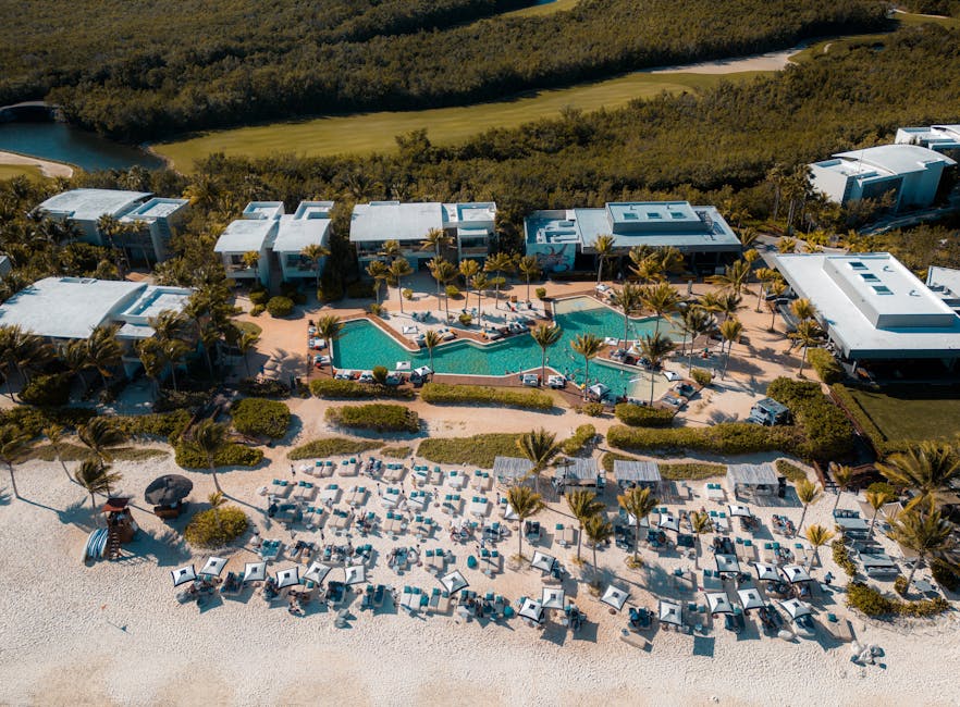 A stunning aerial view of a luxury resort in Playa del Carmen, featuring a large swimming pool and beachside lounging area.
