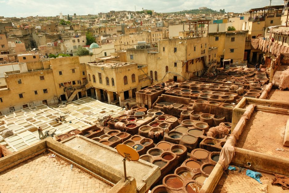 Aerial view of the vibrant traditional tannery in Fes' historic medina, showcasing colorful dye vats and architecture.