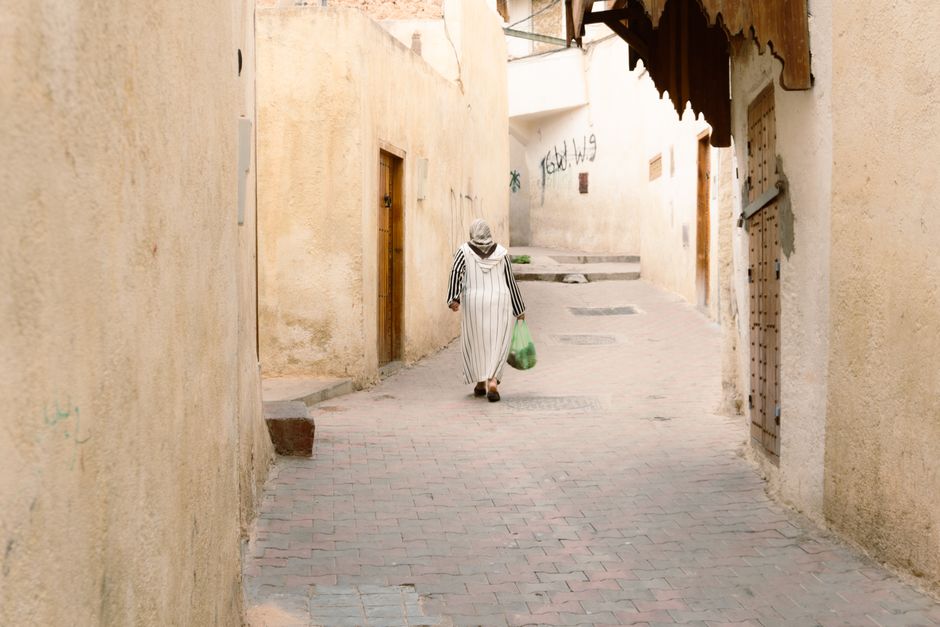A woman in traditional attire walks through a narrow, ancient alleyway with a rustic feel.