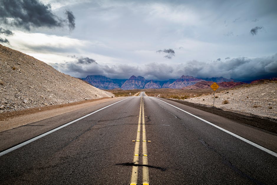 A deserted highway in a barren landscape with mountains under a dramatic sky.
