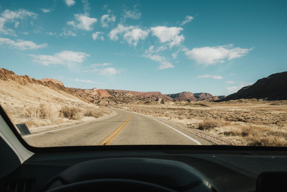View of a winding road through desert mountains from a car interior. Clear blue skies enhance the serene landscape.