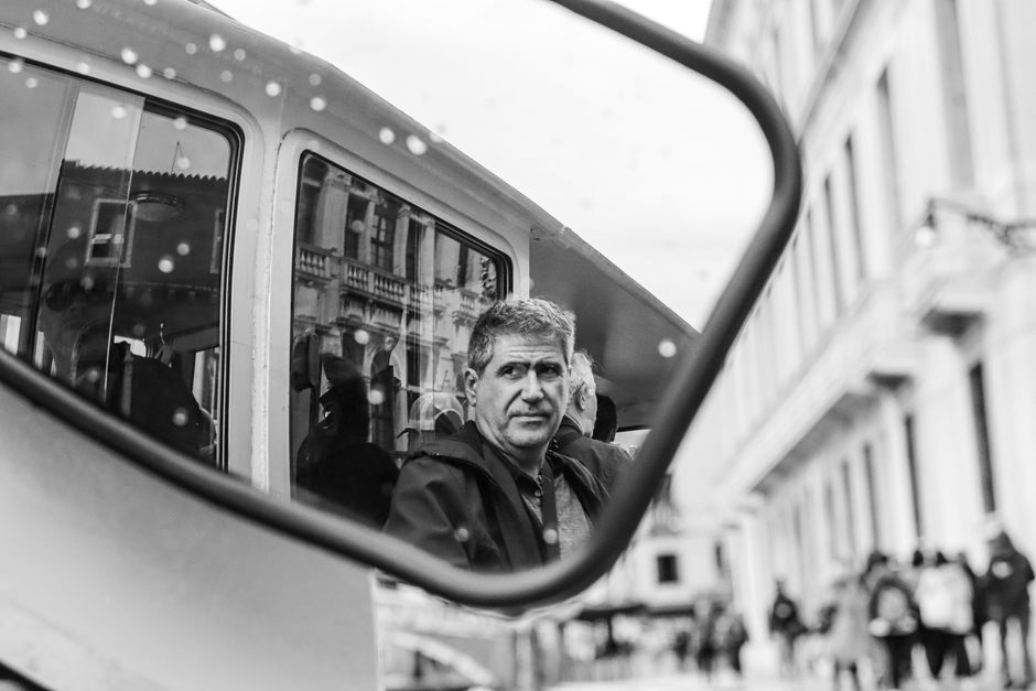 Black and white portrait of a man reflected in a vehicle mirror in Venice, Italy.