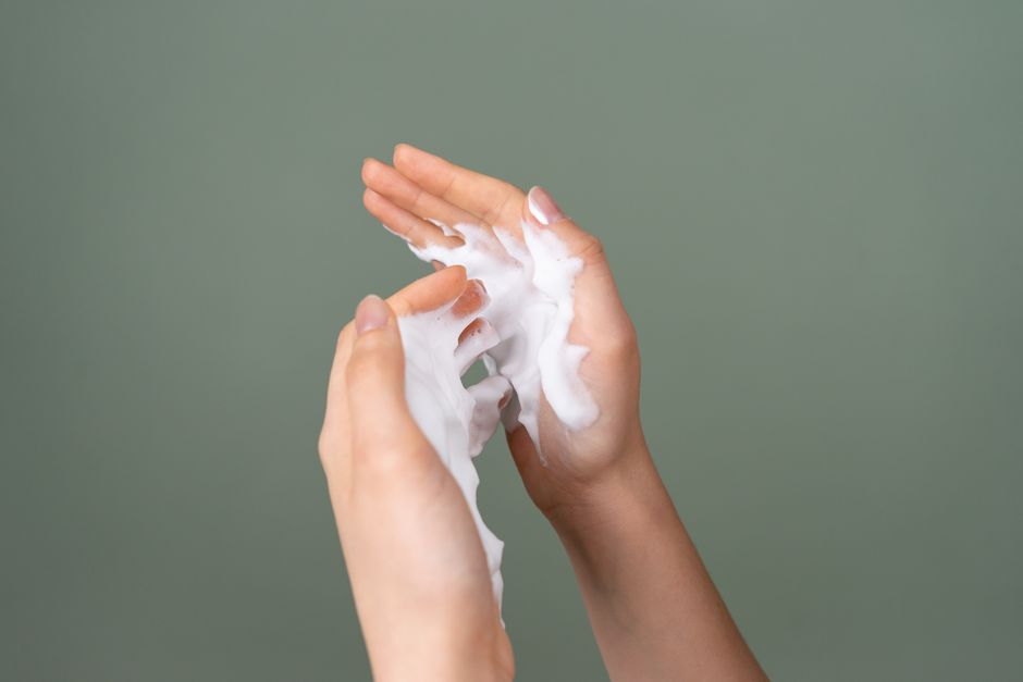 Close-up of hands applying rich moisturizing cream on a green background.