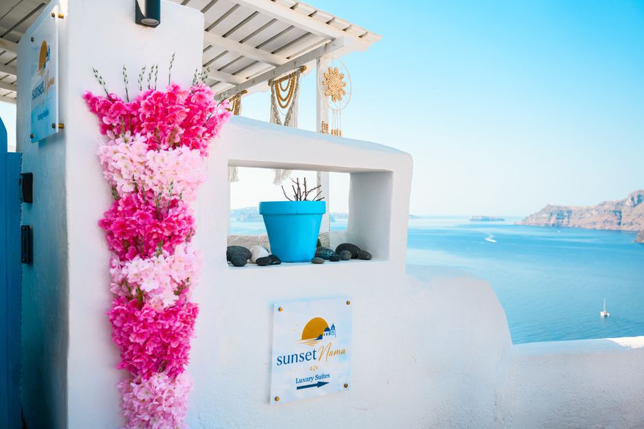 Sun-drenched view from a Santorini luxury suite, showcasing vibrant flowers and stunning ocean backdrop.