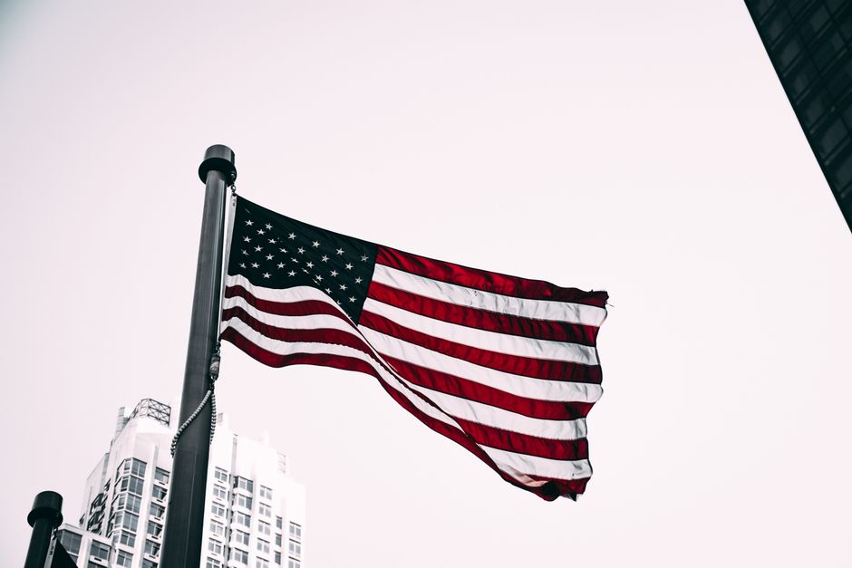 Patriotic image of the American flag waving in the wind with city skyscrapers in the background.