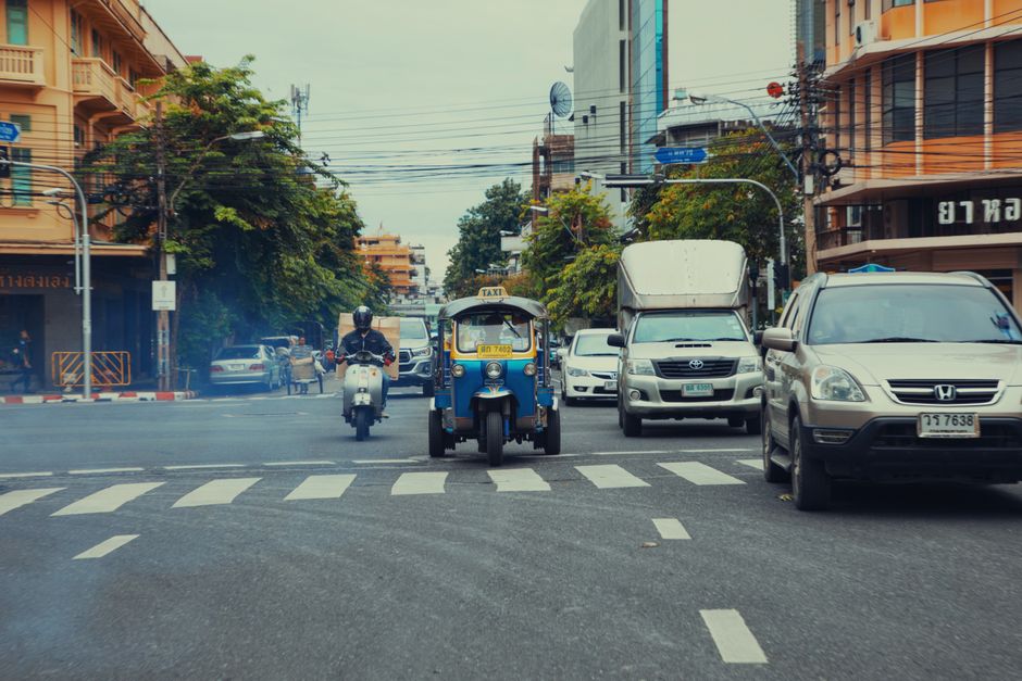 Vibrant street scene in Bangkok featuring a tuk-tuk, motorbikes, and urban traffic.