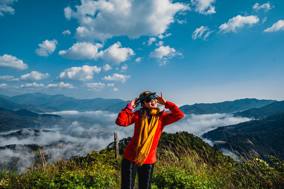 Young traveler posing with peace sign on a mountain with clouds and blue sky.