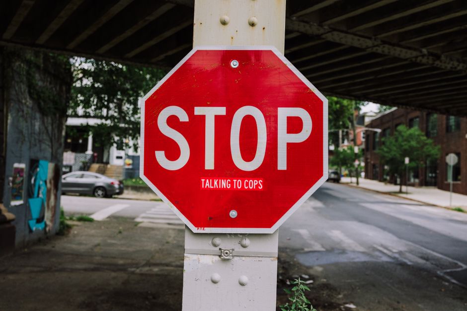A red stop sign with humorous text 'talking to cops' on an urban city street corner.
