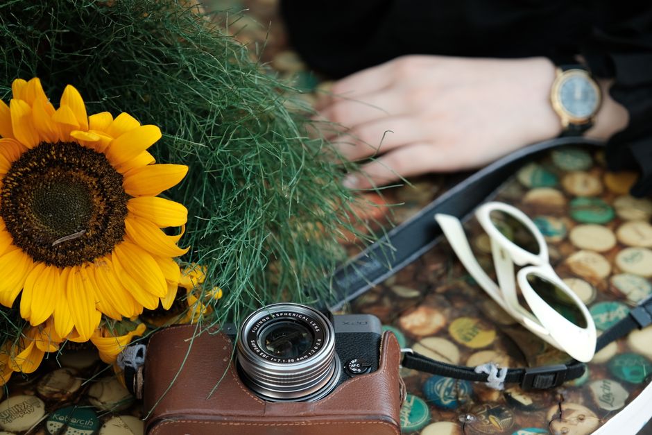 Close-up of a sunflower with a camera and sunglasses on a textured surface.
