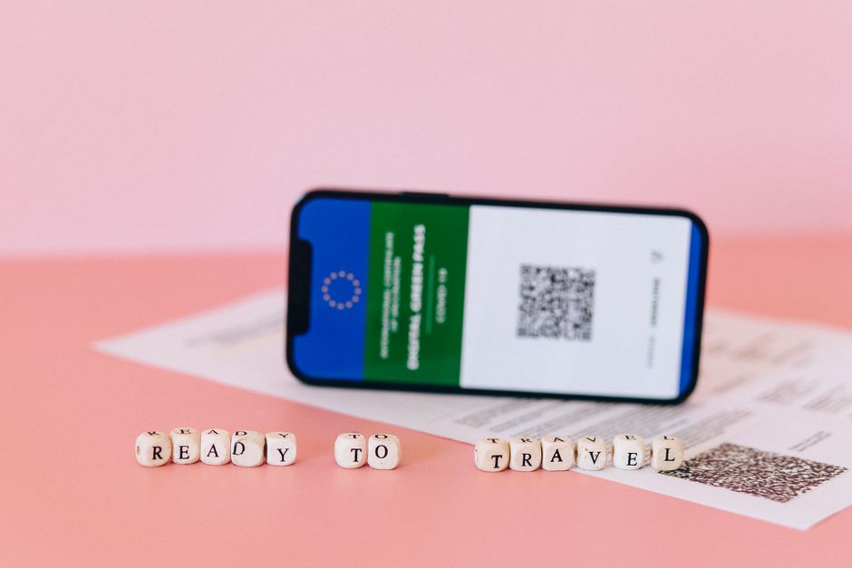 Smartphone displaying digital green pass on a pink surface with travel beads.