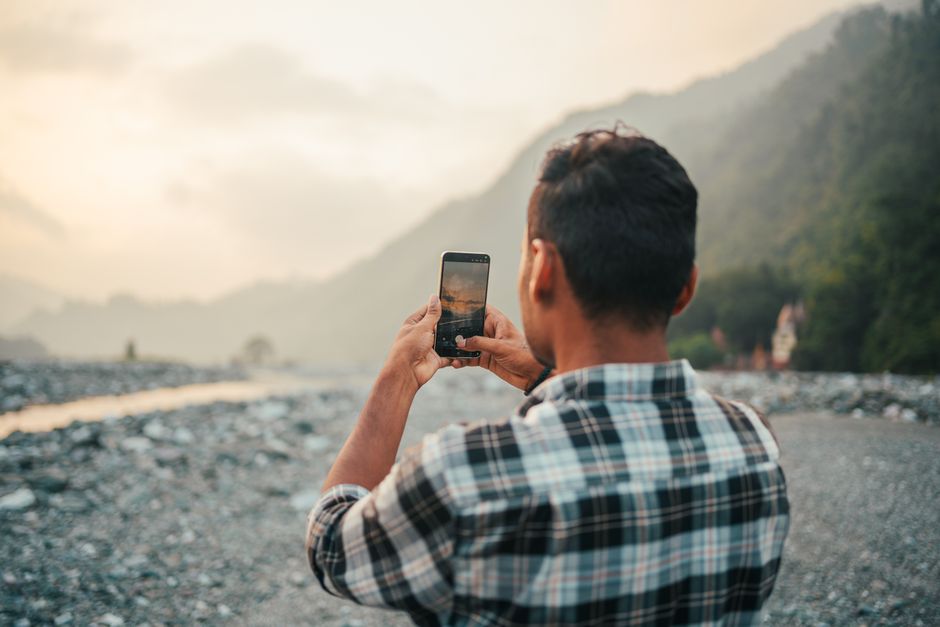 Man takes a photo of a scenic mountain landscape with his smartphone during sunset.