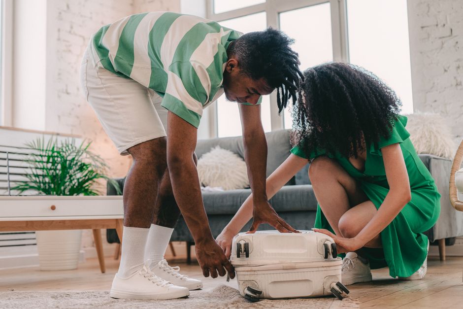 A young couple packing a suitcase in a bright, modern living room, preparing for travel.