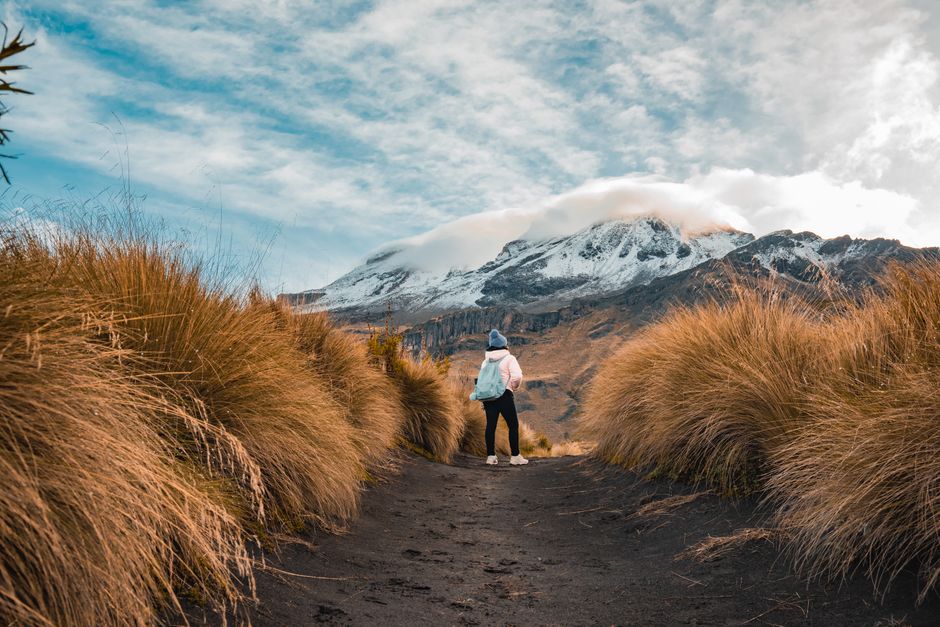 A woman hikes on a path with lush grasses towards Izta-Popo in Mexico.