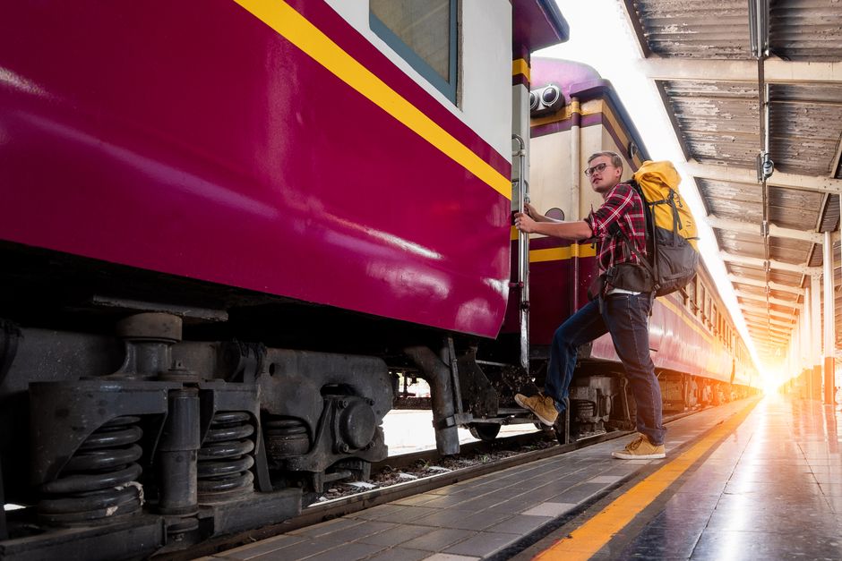 Man with backpack boarding a train at urban railway station during daytime travel adventure.