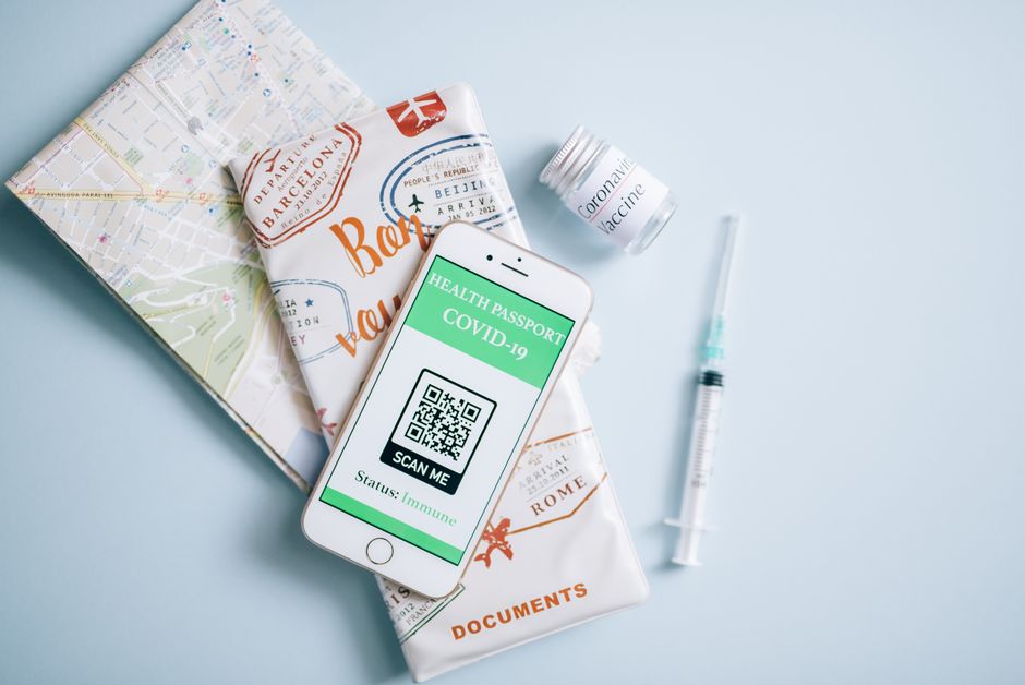 Flat lay of a COVID-19 health passport on a smartphone with vaccine, syringe, and travel documents.