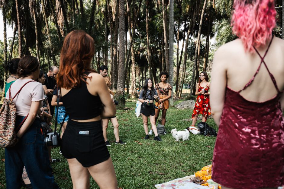 A diverse group of friends gathers outdoors in a park setting, enjoying each other's company amidst tall trees.
